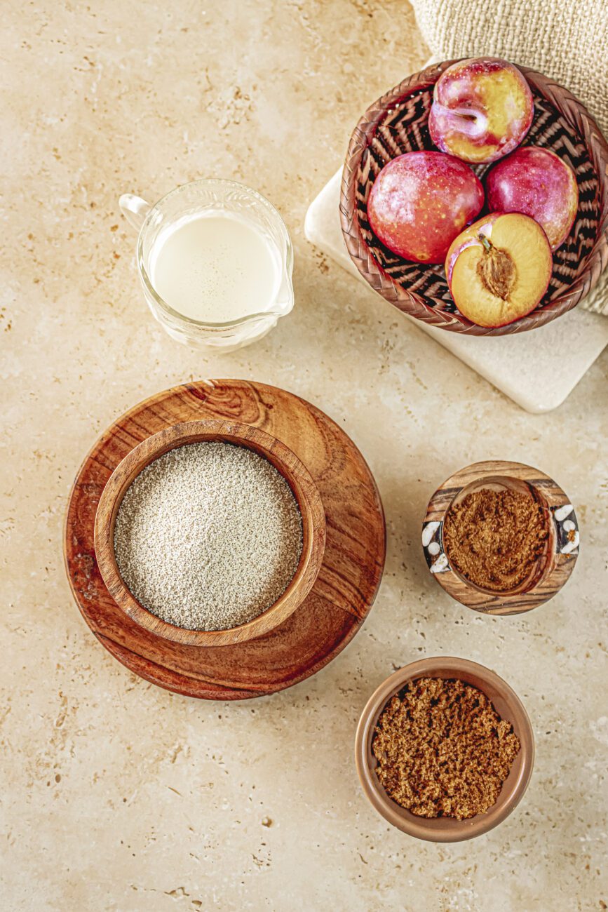 Top View of fonio porridge ingredients, including Fonio grain, spices, brown sugar, cream and plums for a healthy gluten-free breakfast recipe. 