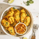 Flat lay of golden Nigerian akara bean fritters served with spicy tomato salsa and garnished with coriander leaves.