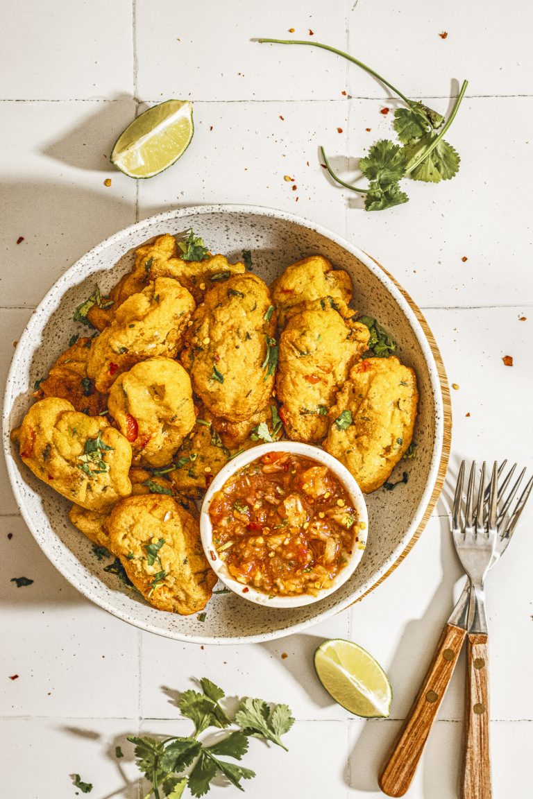 Flat lay of golden Nigerian akara bean fritters served with spicy tomato salsa and garnished with coriander leaves.