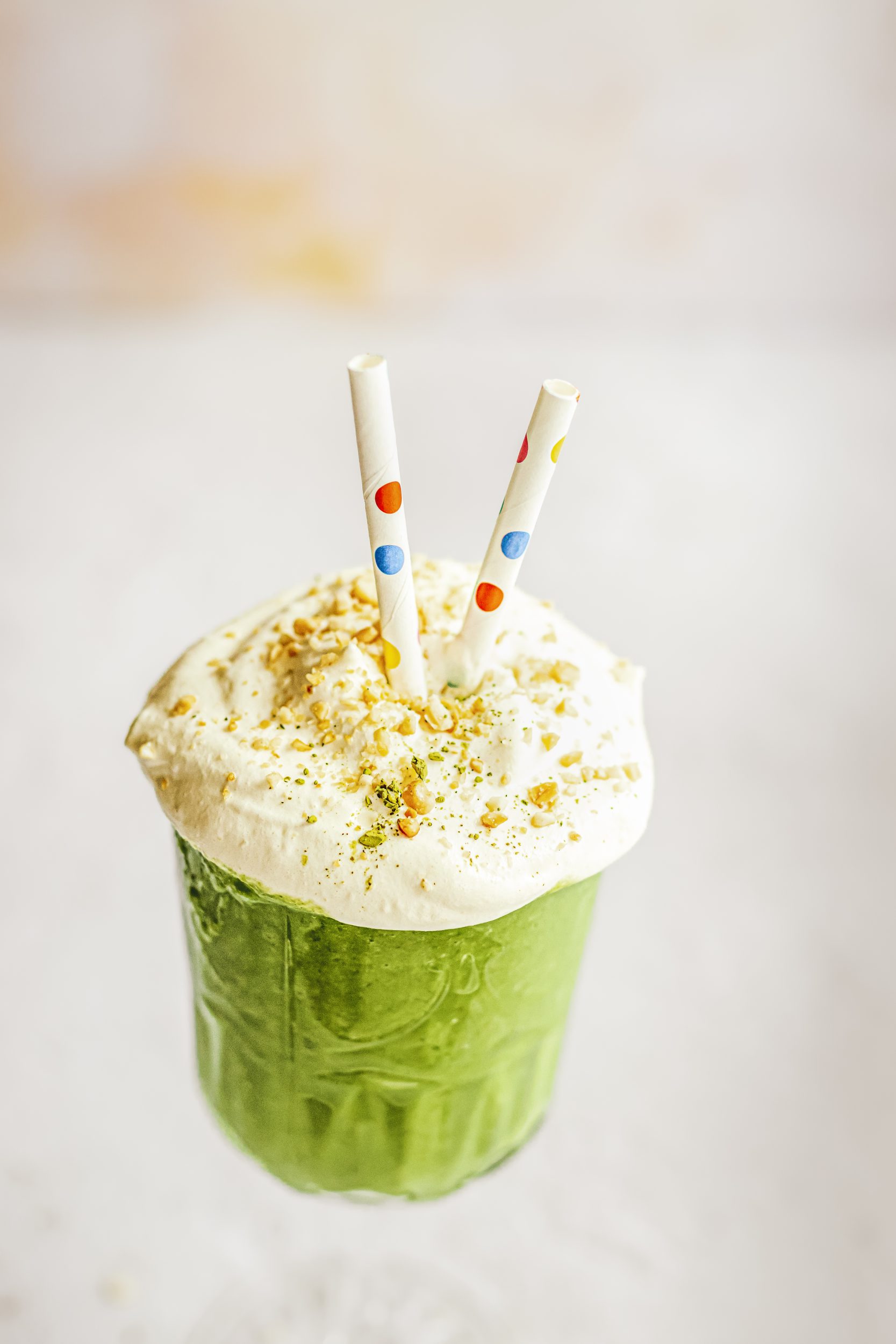 Overhead view of a spinach smoothie topped with cream, nuts, and two colorful paper straws