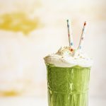 a spinach smoothie topped with cream, nuts, and two colorful paper straws
