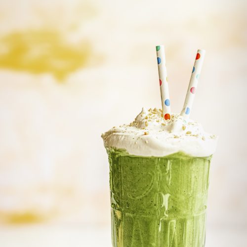 a spinach smoothie topped with cream, nuts, and two colorful paper straws