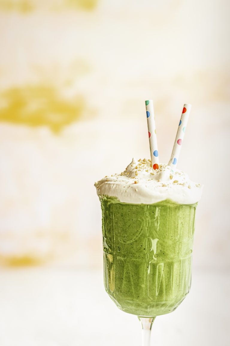 a spinach smoothie topped with cream, nuts, and two colorful paper straws
