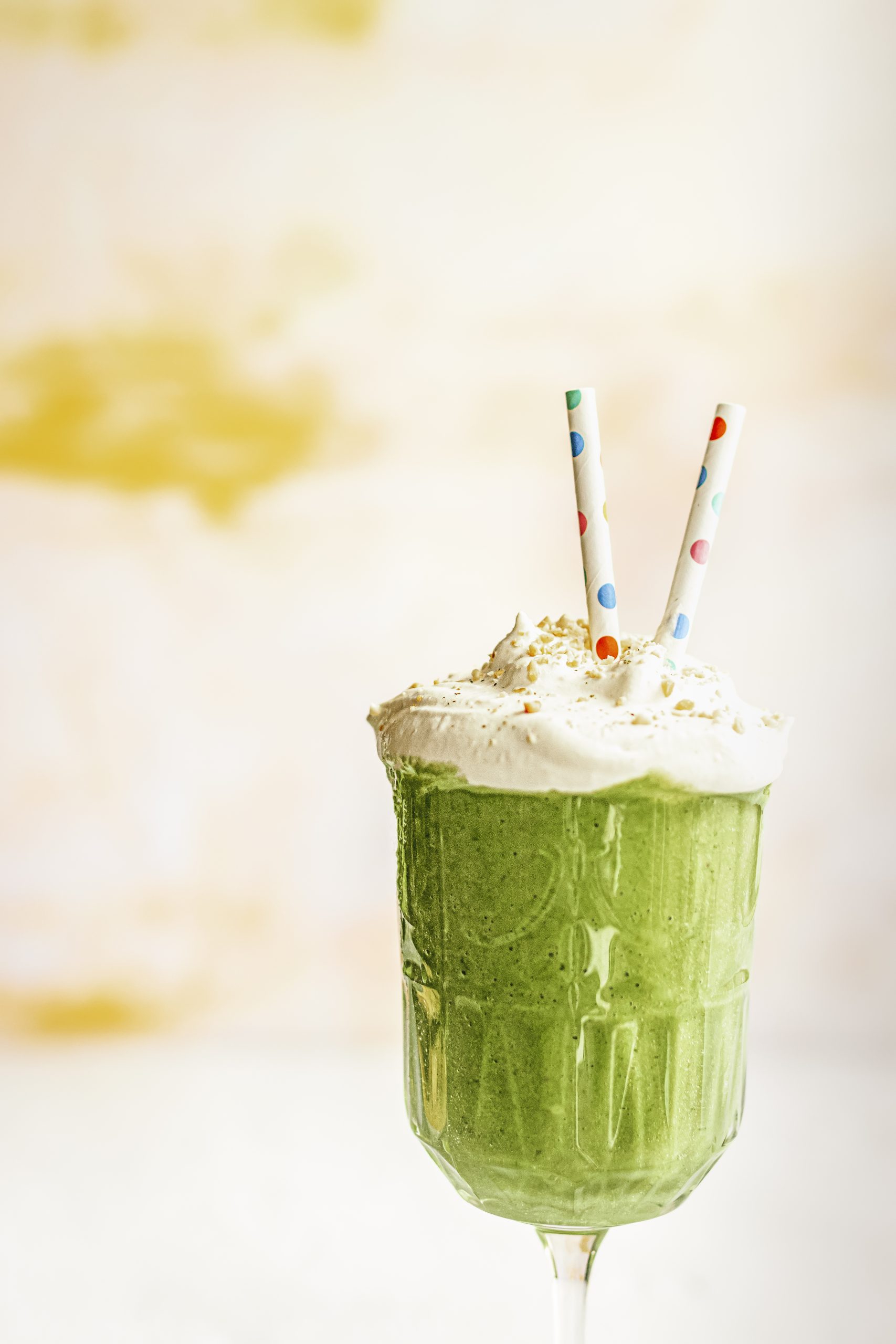 a spinach smoothie topped with cream, nuts, and two colorful paper straws
