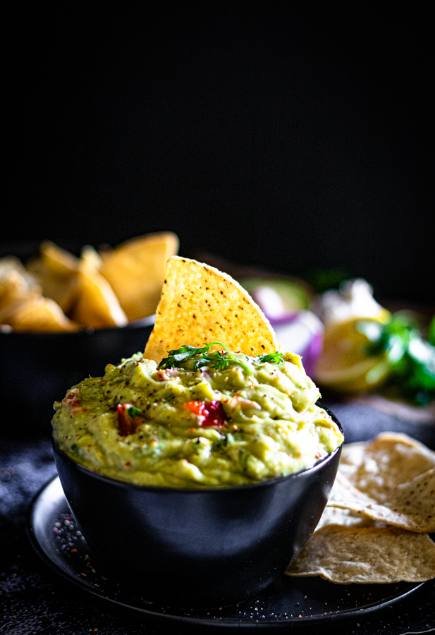 Styled taco night setup featuring a bowl of guacamole surrounded by tacos, ripe avocados, lime wedges, and fresh coriander — an easy guacamole recipe made with wholesome ingredients.