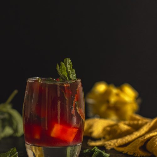 Glass of hibiscus mocktail served over ice and mint leaves, styled with small pineapple chunks. A refreshing non-alcoholic hibiscus drink rich in antioxidants and naturally floral.