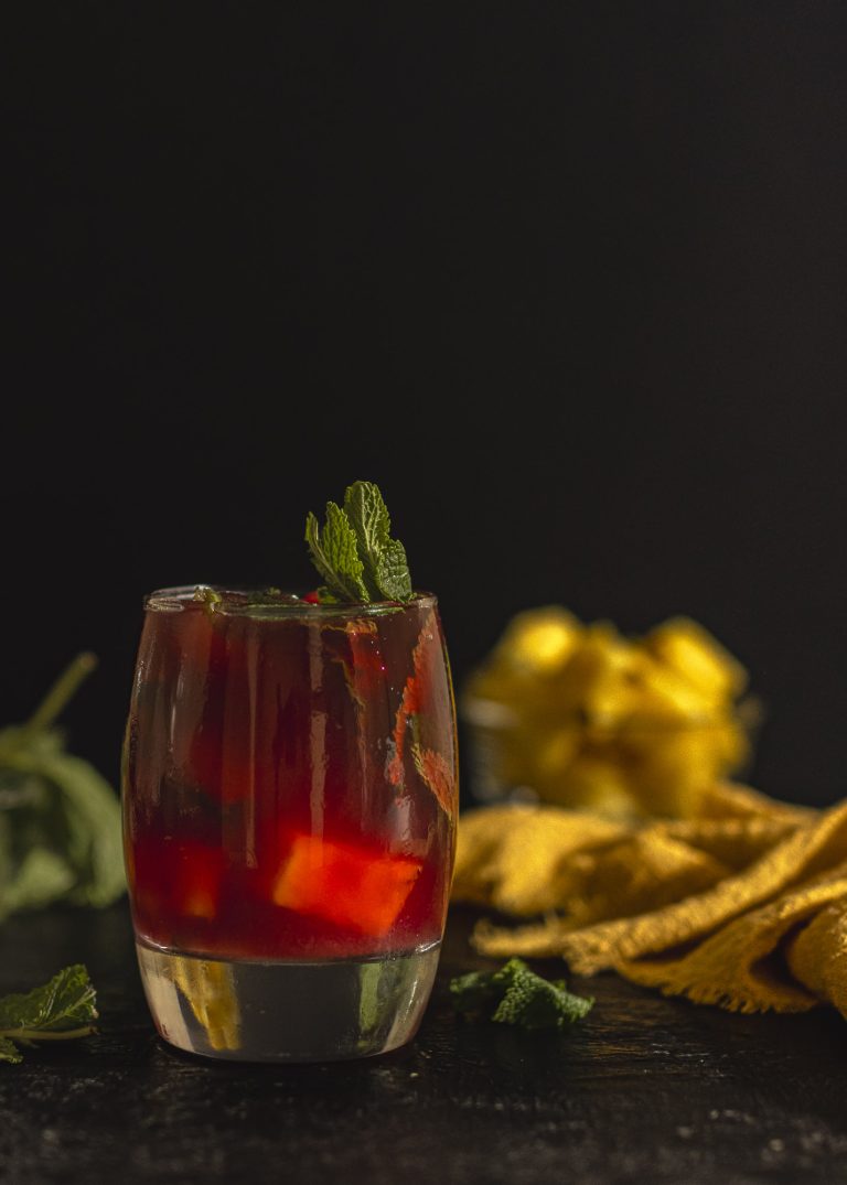 Glass of hibiscus mocktail served over ice and mint leaves, styled with small pineapple chunks. A refreshing non-alcoholic hibiscus drink rich in antioxidants and naturally floral.
