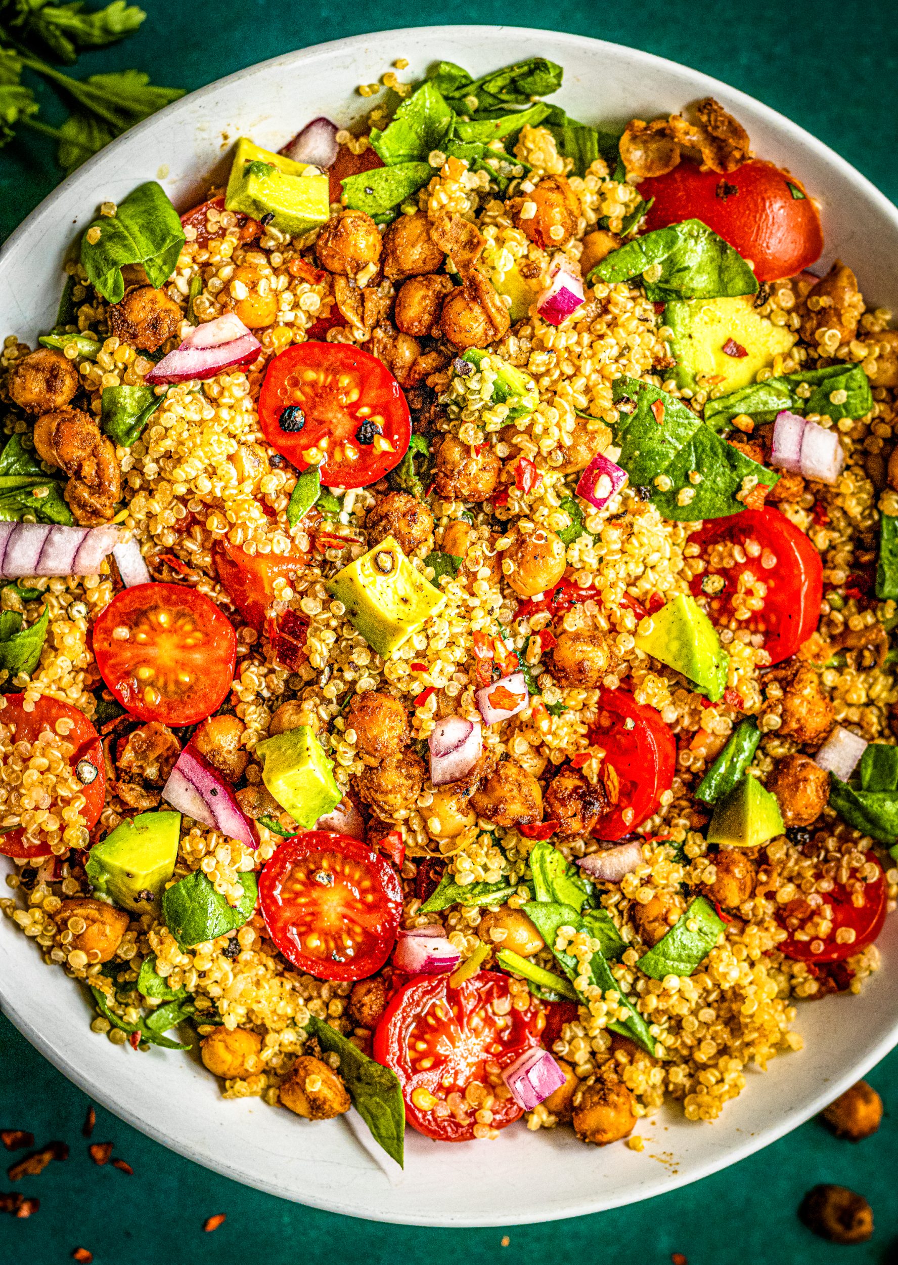 Close-up of quinoa chickpea salad with avocado cubes, cherry tomatoes, and fresh spinach tossed in lemon vinaigrette.
