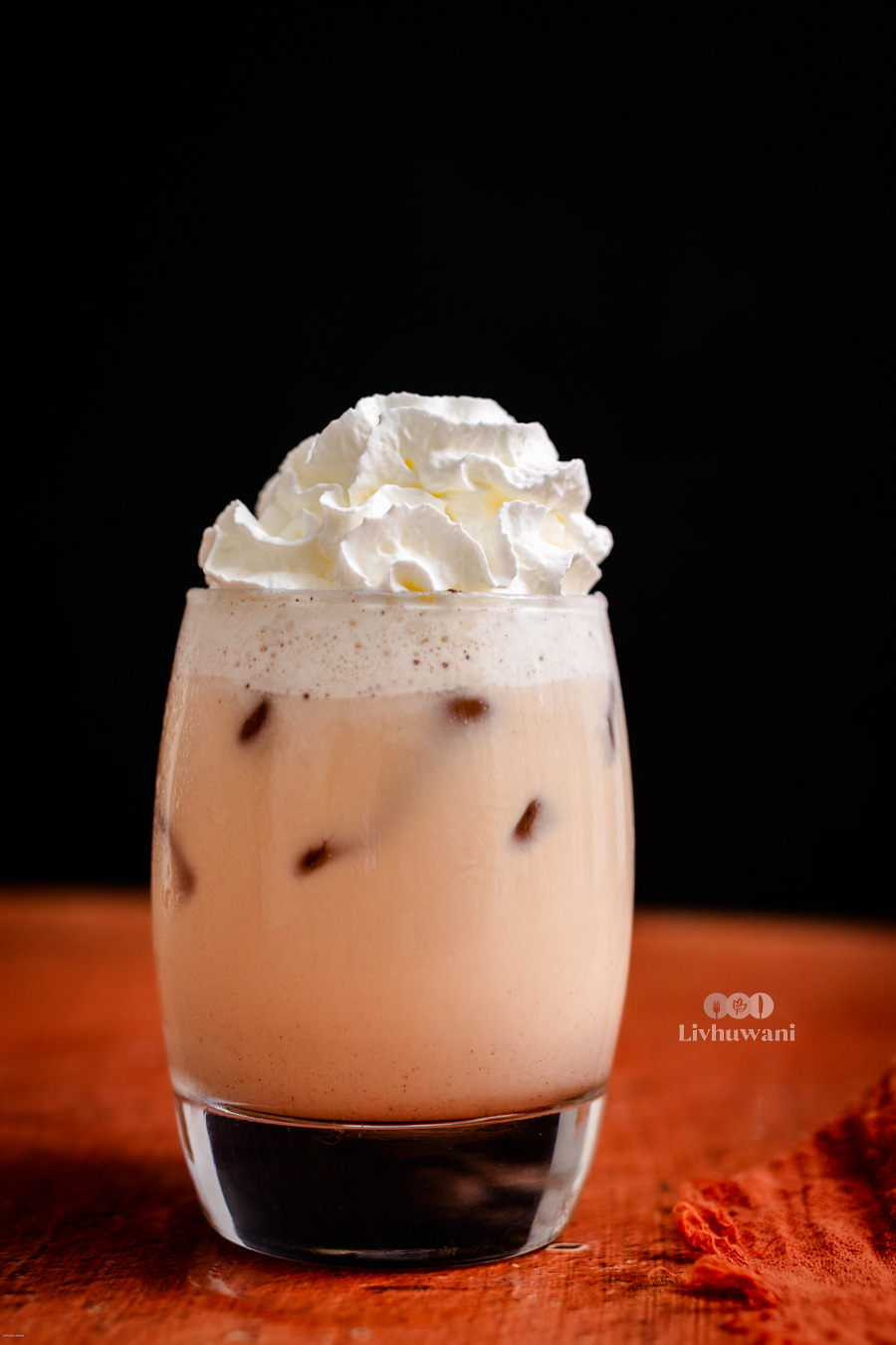 Ice-cold Rooibos tea latte topped with whipped cream in a glass against a dark background, highlighting its creamy and caffeine-free herbal appeal.